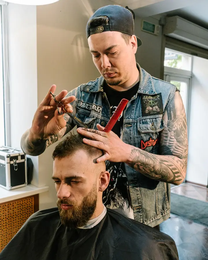 A barber trimming a customer's beard